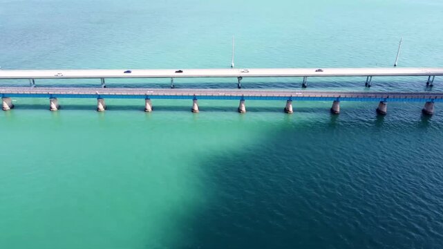 Aerial drone flying parallel to the Seven Mile Bridge Key West Florida, capturing a cinematic sideways view of the iconic span with turquoise Florida Keys water and clear sunny skies.