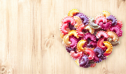 Horizontal banner with Heart formed from uncooked multi-colored pasta on wood texture. Italian food, cuisine, dietary choices, food and love concept. Dried pasta in heart shape. Copy space for text