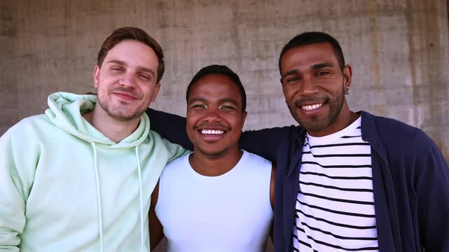Three young, diverse male friends standing together and smiling at the camera with their arms around each other, showcasing a strong bond of friendship, camaraderie, and happiness