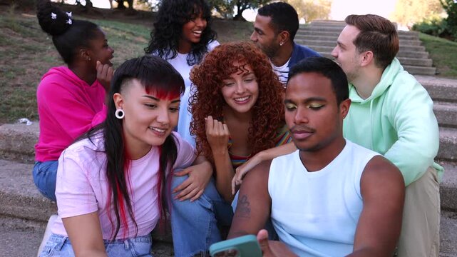 Young multiracial group of friends sitting together on stone stairs in a park, laughing and chatting while looking at a smartphone, celebrating diversity, community, and genuine connection