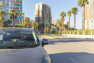 Driver inside car on city street, urban road, traffic sign, modern buildings, transportation concept.