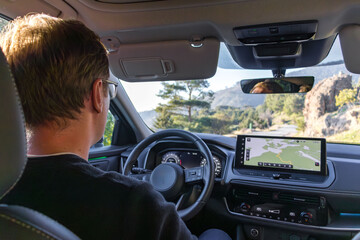 A focused driver sits behind the wheel in a modern car, navigating busy city streets. A large GPS display guides the route, highlighting the tech-enabled, urban driving experience.