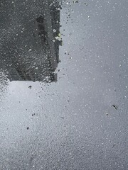 Top view texture of wet asphalt pavement with rain puddle and building reflection