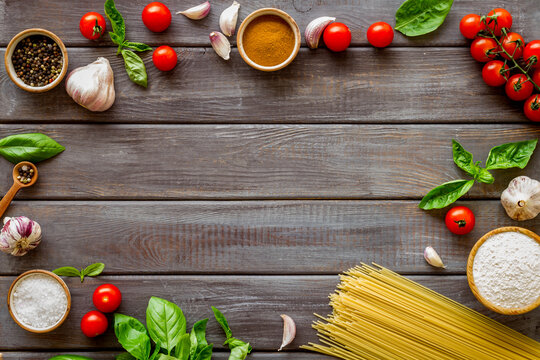 Frame of ingredients for cooking Italian pasta - uncooked spaghetti with tomatoes and basil leaves - on a wooden background, top view - Powered by Adobe