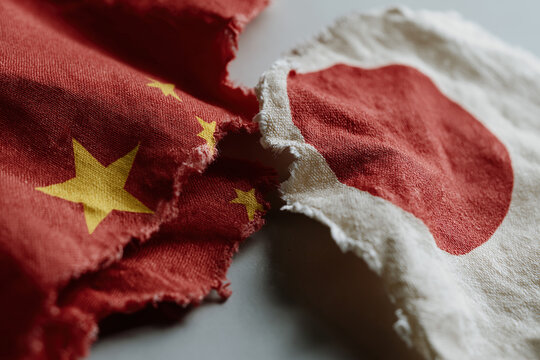 Torn Chinese and Japanese flags symbolizing strained diplomatic relations between nations.