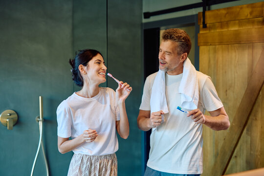 Cheerful couple enjoying their morning routine together, brushing teeth in a modern bathroom, showing wellness and togetherness - Powered by Adobe