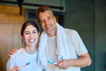 Fototapeta premium Happy couple smiling and holding toothbrushes, preparing for their daily dental care and hygiene routine in the bathroom