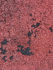 Top view texture of worn red rubber running track or synthetic playground surface with black spots