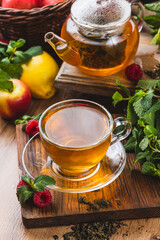 Tea in a glass mug on the table next to mint, raspberries and fruits