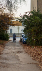 man walking with chidren stroller along autumn path near parked cars