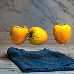  three fresh persimmons floating above blue cloth on wooden surface