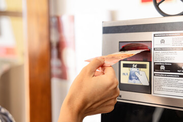 Funchal, Portugal - November 11, 2025: Hand inserting cash into payment machine at public transport station