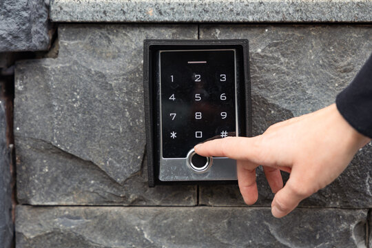 Hand pressing keypad on modern security system mounted on stone wall with sleek design