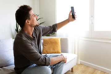 Young man using phone relaxing sitting on the sofa taking selfie. Copy space.