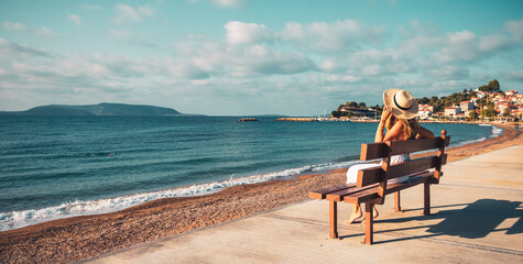 a woman wearing white dress sitting on a bench looking at the sea