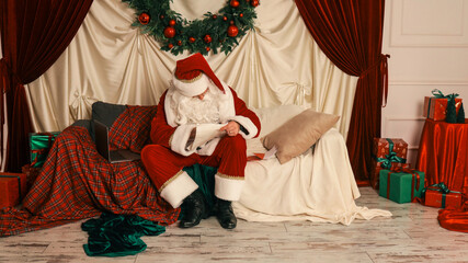 Santa Claus reviews his list while relaxing on a couch before Christmas