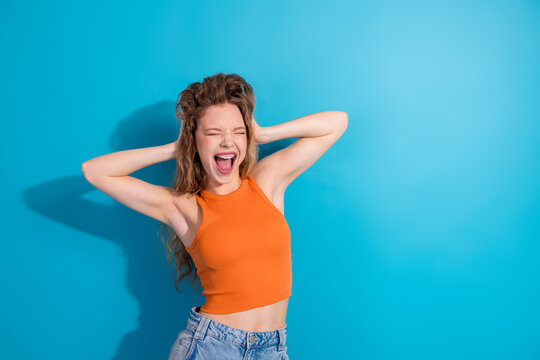 Young woman in orange crop top poses joyfully against blue background for lifestyle fashion shoot highlighting happiness and casual style