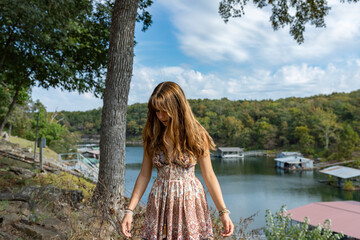 teenaged female in dress standing on hill near lake