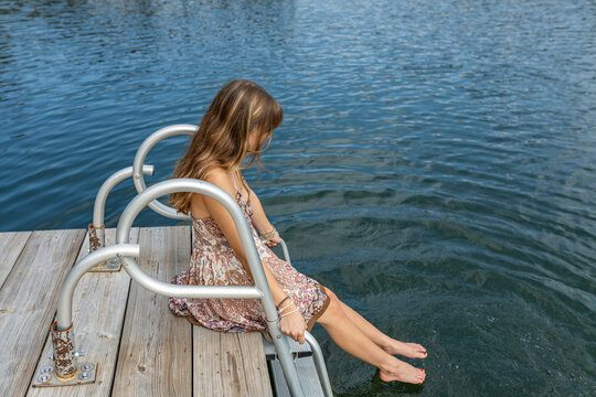 teenager in dress sitting on swim dock with feet in water