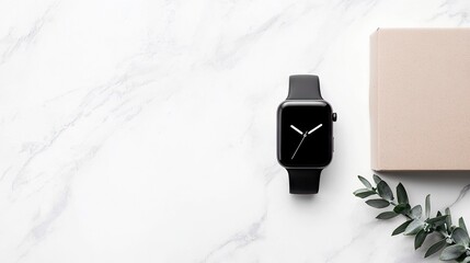 A black smartwatch with a minimalist clock face sits on a white marble surface next to a light brown box and a sprig of green leaves.