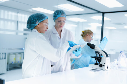 A pharmaceutical Quality Control QC team ensures GxP compliance. Two scientists review an electronic batch record on a tablet while a third performs a required analytical test. - Powered by Adobe