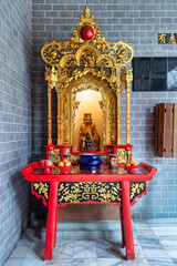 Ornate golden shrine with a statue, offerings, and red altar table inside Chan She Shu Yuen Ancestral Hall, Kuala Lumpur, Malaysia. Traditional Chinese cultural interior