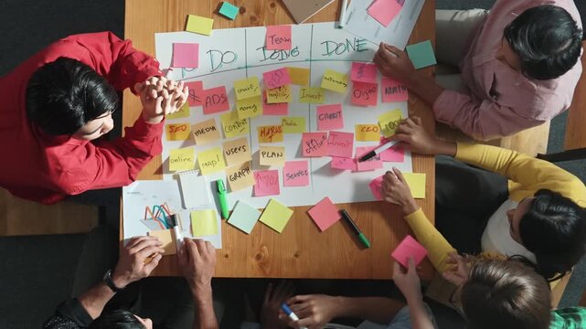 Top view of people writing and making scrum task board or kanban board while writing plan and planning strategy at colorful sticky notes. Team putting hand together and clapping hands. Convocation.