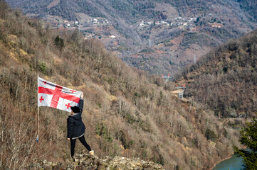 A traveler lifting a Georgian flag on a mountain ridge overlooking the countryside of Georgia.