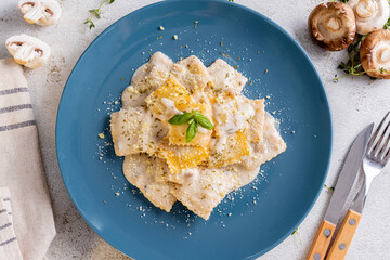 a plate of ravioli, filled with a butternut squash mixture, served in a creamy white sauce. It is garnished with grated Parmesan cheese, dried herbs, and a fresh basil leaf, with fresh mushroom