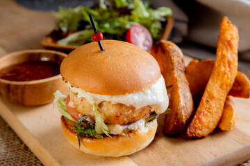 a juicy, cheesy chicken burger served with thick-cut potato wedges and a fresh side salad. The burger features a thick chicken patty topped with melted white cheese, lettuce, tomato and bun