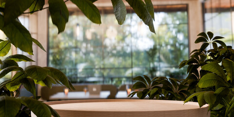 Empty wooden podium with green leaves on blurry interior background for natural product placement, rustic wood stage for eco cosmetic or food display.