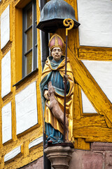 Close-up of a bishop statue mounted on a yellow timber-frame house in historic Nuremberg.