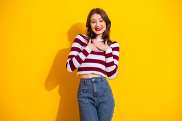 Bright young woman in striped burgundy and white top smiles against yellow background casual...
