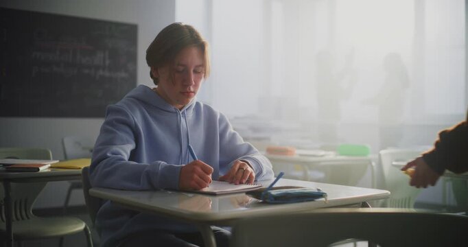 Teen Boy in Blue Hoodie Sits Alone at Desk, Lost in Thought, as Female Classmate Walking by Quietly Leaves Apple Core on Desk. Concept Teenage Loneliness, Silent Connection, and Emotional Distance.
