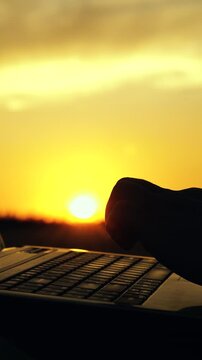 Laptop in hands of businessman outdoors, close-up. Businessman farmer with laptop working on field, estimating grain harvest. Farmer man working on computer, sunset. Agricultural business concept