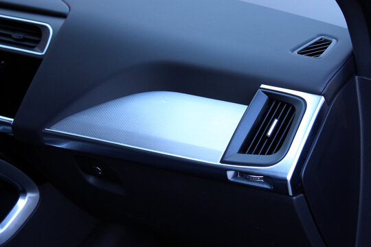 Black glove box with silver trim, black leather dashboard, and silver-framed air vent design, show modern premium cabin details. Front Passenger airbag. Glove compartment. Car air conditioning.