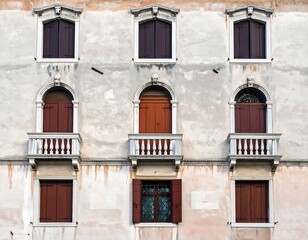 A close-up of a weathered, six-windowed facade with dark shutters and decorative balconies. The building shows age and patina