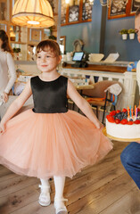 Girl in a black and pink dress holds cake in cafe