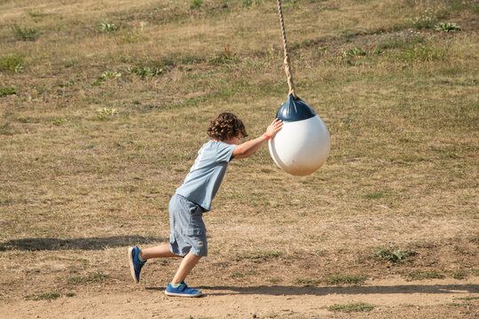 Young boy pushing a hanging swing ball outdoors in a natural adventure park on a sunny day