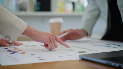 Close-up of two business women analyzing financial data on charts and laptop screen during a team meeting - Powered by Adobe