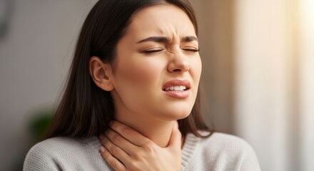 Woman grimaces while holding her throat in discomfort indoors.