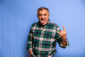 Senior man showing rock and roll gesture sticking out tongue