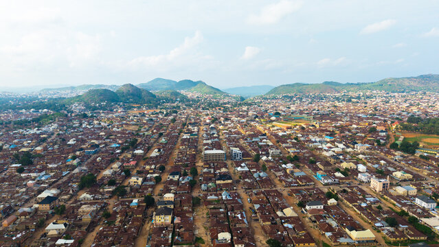 Aerial view of the city's grid-like streets stretching towards rolling green hills under a soft sky, a vibrant tapestry of urban life, Jos, Plateau, Nigeria.