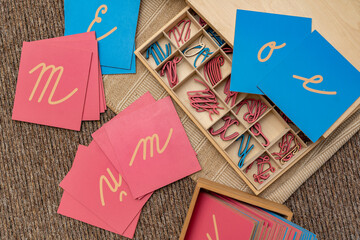Montessori writing materials. Sensory materials, pink and blue letter cards and cut out letters in a wooden tray. Alternative writing instruction.