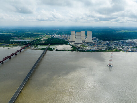 Aerial view of a bridge stretching across the wide, reflective river towards the towering nuclear plant structures against the horizon, Ruppur, Rajshahi Division, Bangladesh.
