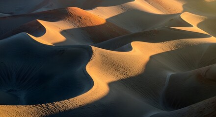 Stunning close-up of sand dunes in the desert, highlighting the dramatic contrast between sunlit, warm curves and deep, long shadows during sunrise or sunset.