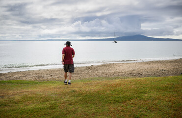 Man walking on the beach. Clouds covering Rangitoto Island. Auckland.
