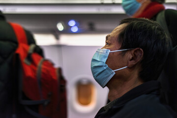 Man wearing a face mask on the airplane. Indistinctive passengers walking along the aisle.