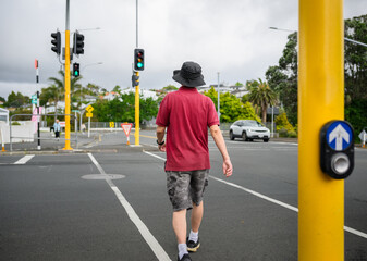 Man walking across the street with green pedestrian crossing light on. Auckland.