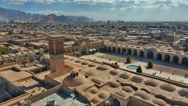 Aerial view of the Ganjali Khan Complex's honeycombed domes and towering windcatcher, a symphony of earthen hues against the city's sprawling tapestry, Kerman, Kerman Province, Iran.